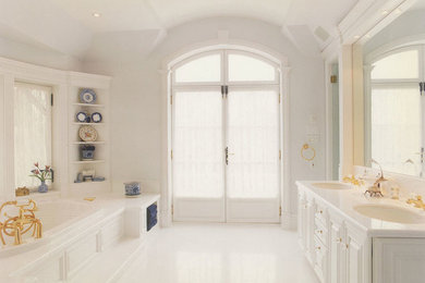 Example of a large classic master drop-in bathtub design in Montreal with raised-panel cabinets, white cabinets, white walls, an undermount sink and solid surface countertops