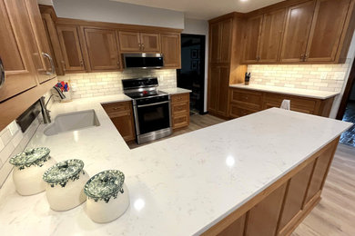 Mid-sized u-shaped vinyl floor kitchen photo in Kansas City with an undermount sink, shaker cabinets, medium tone wood cabinets, quartz countertops, white backsplash, subway tile backsplash, stainless steel appliances and white countertops