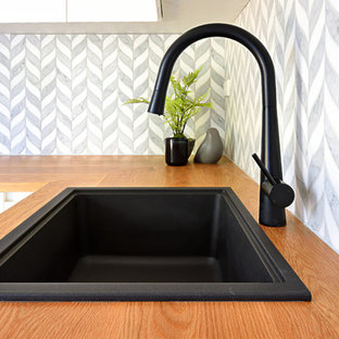 シドニーの小さいモダンスタイルのおしゃれな洗濯室 (アンダーカウンターシンク、ガラス扉のキャビネット、白いキャビネット、木材カウンター、グレーの壁、セラミックタイルの床、左右配置の洗濯機・乾燥機、グレーの床、茶色いキッチンカウンター) の写真