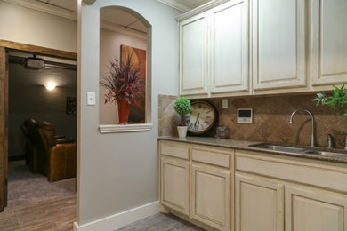Photo of a small traditional single-wall wet bar in Dallas with an undermount sink, raised-panel cabinets, beige cabinets, granite benchtops, brown splashback, ceramic splashback, porcelain floors, grey floor and grey benchtop.