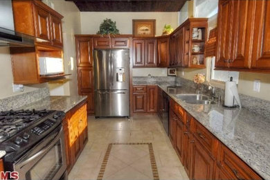 Mid-sized elegant u-shaped ceramic tile eat-in kitchen photo in Los Angeles with a double-bowl sink, raised-panel cabinets, dark wood cabinets, granite countertops, stainless steel appliances and no island
