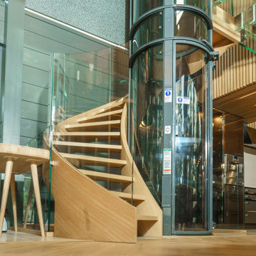 Bogentreppen aus Holz mit Glasgeländer, Fahrstuhl und Glasbrücke - Siller Treppe