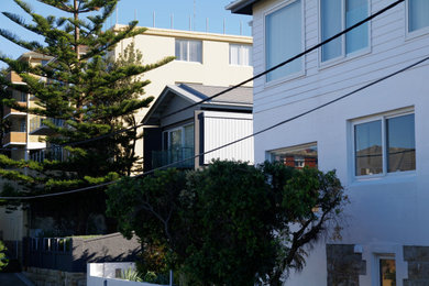 Photo of a three-storey stucco grey house exterior in Sydney with a gable roof and a shingle roof.