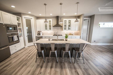 Large transitional laminate floor and brown floor kitchen photo in Cedar Rapids with a farmhouse sink, shaker cabinets, white cabinets, quartzite countertops, stainless steel appliances and an island