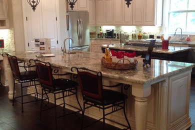 Example of a large trendy l-shaped dark wood floor open concept kitchen design in Dallas with raised-panel cabinets, beige cabinets, granite countertops, two islands, an undermount sink, beige backsplash, stone tile backsplash and stainless steel appliances