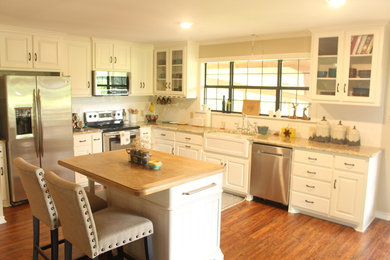 Mid-sized country l-shaped laminate floor and orange floor eat-in kitchen photo in Austin with a farmhouse sink, raised-panel cabinets, white cabinets, granite countertops, white backsplash, subway tile backsplash, stainless steel appliances and an island