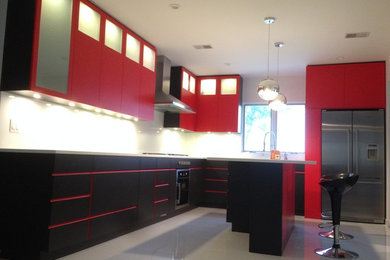 Inspiration for a mid-sized modern l-shaped eat-in kitchen remodel in New York with a double-bowl sink, flat-panel cabinets, red cabinets, glass countertops, white backsplash, glass sheet backsplash, stainless steel appliances and an island