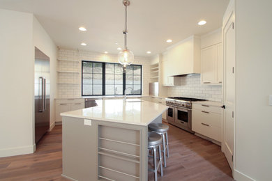 Inspiration for a large contemporary u-shaped medium tone wood floor and brown floor enclosed kitchen remodel in Other with an integrated sink, flat-panel cabinets, white cabinets, solid surface countertops, white backsplash, subway tile backsplash, stainless steel appliances and an island