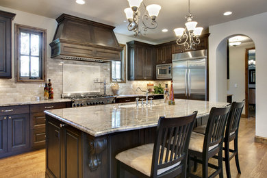 Inspiration for a large timeless single-wall medium tone wood floor and brown floor open concept kitchen remodel in Los Angeles with an undermount sink, dark wood cabinets, granite countertops, gray backsplash, stone tile backsplash, stainless steel appliances, an island and raised-panel cabinets