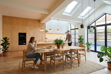 Large contemporary kitchen/dining room in London with light hardwood flooring, a vaulted ceiling, white walls and beige floors.