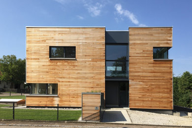 Photo of a mid-sized contemporary two-storey exterior in Munich with wood siding and a flat roof.