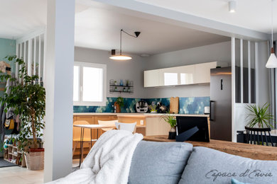 Exemple d'une cuisine ouverte scandinave en L et bois clair de taille moyenne avec un évier encastré, un placard à porte plane, un plan de travail en stratifié, une crédence bleue, un électroménager noir, îlot et un plan de travail blanc.