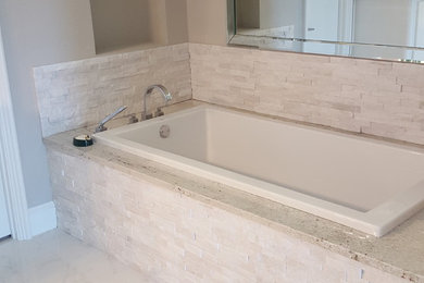 Cette photo montre une salle de bain principale tendance de taille moyenne avec des portes de placard blanches, une baignoire posée, un carrelage beige, des dalles de pierre, un mur beige, un sol en marbre, un plan de toilette en surface solide et un placard à porte plane.