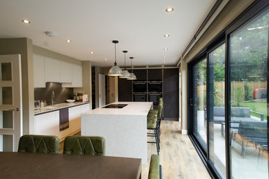 Inspiration for a mid-sized modern l-shaped open plan kitchen in Surrey with laminate floors, brown floor, a drop-in sink, flat-panel cabinets, white cabinets, solid surface benchtops, with island and white benchtop.