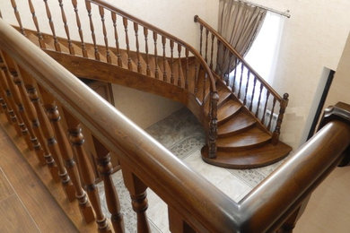 Стильный дизайн: большая изогнутая деревянная лестница в классическом стиле с деревянными ступенями и деревянными перилами - последний тренд