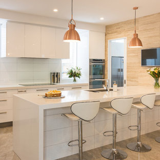 This is an example of a large modern galley kitchen pantry in Christchurch with an undermount sink, white cabinets, granite benchtops, white splashback, travertine splashback, stainless steel appliances, porcelain floors, with island and beige floor.
