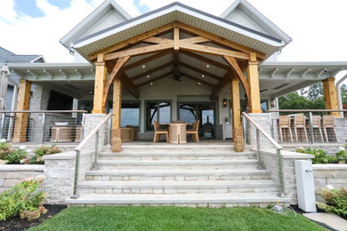 This is an example of a large traditional stone cable railing porch design in Other with a roof extension.