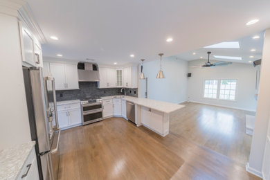 Open concept kitchen - transitional dark wood floor and brown floor open concept kitchen idea in New York with an undermount sink, shaker cabinets, white cabinets, quartzite countertops, black backsplash, stone tile backsplash, stainless steel appliances and gray countertops