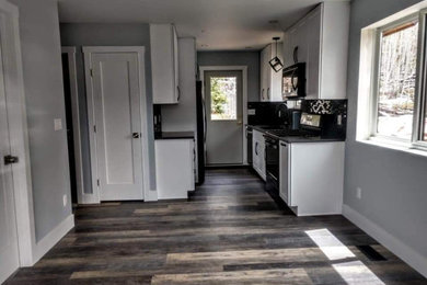Example of a small minimalist vinyl floor and multicolored floor eat-in kitchen design in Other with an undermount sink, shaker cabinets, white cabinets, quartzite countertops, black backsplash, glass tile backsplash, black appliances and black countertops