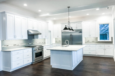 This is an example of a large traditional l-shaped eat-in kitchen in Other with an undermount sink, recessed-panel cabinets, white cabinets, quartz benchtops, grey splashback, ceramic splashback, stainless steel appliances, dark hardwood floors, with island, brown floor and white benchtop.