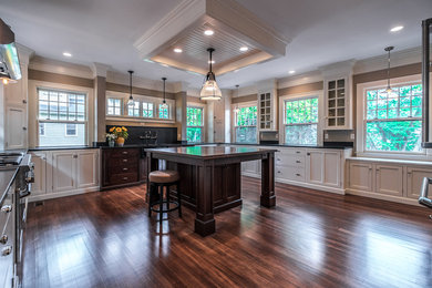 Large elegant u-shaped medium tone wood floor and brown floor enclosed kitchen photo in Boston with white cabinets, granite countertops, stainless steel appliances, an island, a farmhouse sink, black backsplash, stone slab backsplash and shaker cabinets