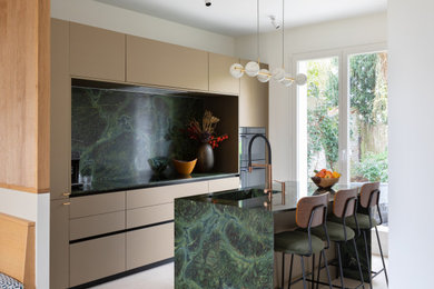 Idée de décoration pour une cuisine parallèle design avec un évier intégré, un placard à porte plane, des portes de placard beiges, une crédence verte, une crédence en dalle de pierre, un électroménager noir, îlot, un sol beige et un plan de travail vert.