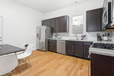 Example of a mid-sized trendy l-shaped medium tone wood floor eat-in kitchen design in Chicago with an undermount sink, shaker cabinets, brown cabinets, granite countertops, white backsplash, mosaic tile backsplash, stainless steel appliances, no island and beige countertops