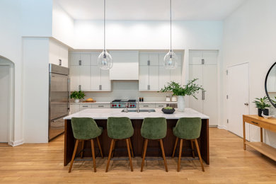 Open concept kitchen - mid-sized modern l-shaped light wood floor open concept kitchen idea in Chicago with an undermount sink, flat-panel cabinets, white cabinets, quartz countertops, white backsplash, ceramic backsplash, stainless steel appliances, an island and white countertops