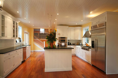 Large transitional galley medium tone wood floor eat-in kitchen photo in Philadelphia with a drop-in sink, recessed-panel cabinets, white cabinets, granite countertops, gray backsplash, stainless steel appliances and an island