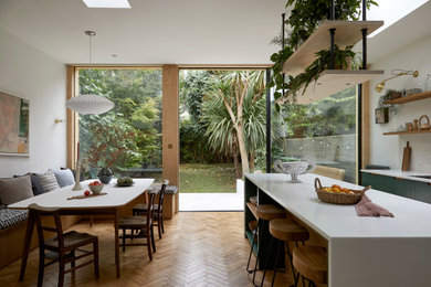Large retro dining room in London with banquette seating, white walls and medium hardwood flooring.