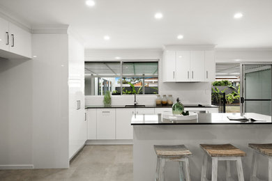 Photo of a mid-sized contemporary l-shaped kitchen pantry in Sunshine Coast with an undermount sink, flat-panel cabinets, white cabinets, quartz benchtops, white splashback, subway tile splashback, stainless steel appliances, porcelain floors, with island, grey floor, grey benchtop and timber.