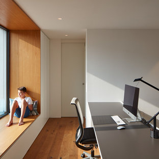 Medium sized modern home studio in Stuttgart with white walls, light hardwood flooring, no fireplace, a built-in desk and brown floors.