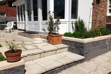 This is an example of a mid-sized traditional backyard patio in Sydney with a container garden, natural stone pavers and no cover.