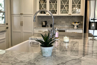 Mid-sized elegant l-shaped porcelain tile and brown floor eat-in kitchen photo in Santa Barbara with a farmhouse sink, shaker cabinets, white cabinets, marble countertops, white backsplash, marble backsplash, stainless steel appliances, an island and multicolored countertops