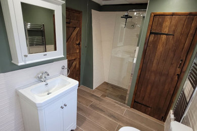 This is an example of a large traditional bathroom in Essex with shaker cabinets, white cabinets, a freestanding bath, a walk-in shower, a two-piece toilet, white tiles, ceramic tiles, green walls, porcelain flooring, a built-in sink, brown floors, an open shower, a chimney breast, a single sink, a freestanding vanity unit and exposed beams.