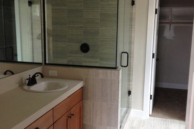Mid-sized transitional 3/4 gray tile and porcelain tile porcelain tile and gray floor corner shower photo in Other with shaker cabinets, medium tone wood cabinets, beige walls, a drop-in sink, quartz countertops, a hinged shower door and beige countertops