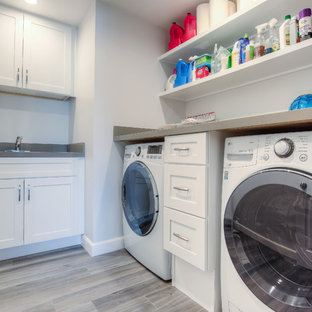 ロサンゼルスの中サイズのトランジショナルスタイルのおしゃれな洗濯室 (シェーカースタイル扉のキャビネット、白いキャビネット、白い壁、左右配置の洗濯機・乾燥機、アンダーカウンターシンク、コンクリートカウンター、ラミネートの床、茶色い床) の写真