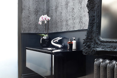 Inspiration for a mid-sized eclectic powder room in London with an integrated sink, flat-panel cabinets, black cabinets, glass benchtops, grey walls and limestone floors.
