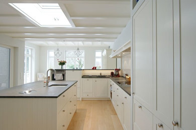 Design ideas for a country kitchen in Hamburg with an undermount sink, shaker cabinets, white cabinets, white splashback, ceramic splashback, light hardwood floors and with island.