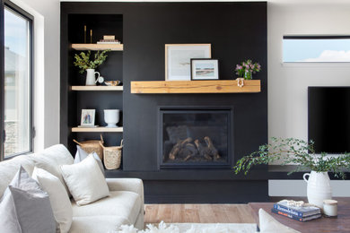 他の地域にあるお手頃価格の北欧スタイルのおしゃれなリビング (黒い壁、淡色無垢フローリング、標準型暖炉、表し梁) の写真