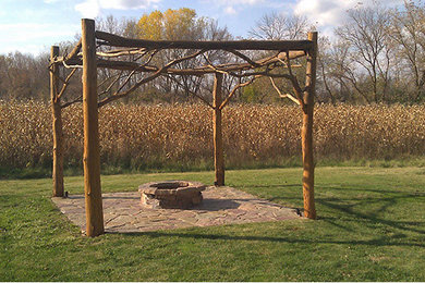 This is an example of a mid-sized country backyard patio in Milwaukee with a fire feature, natural stone pavers and a pergola.