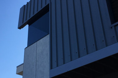Photo of a contemporary two-storey black exterior in Townsville with metal siding, a flat roof and a metal roof.