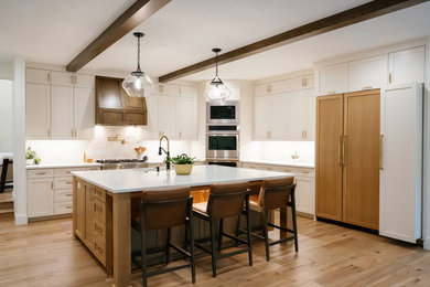 Example of a large trendy l-shaped medium tone wood floor and brown floor enclosed kitchen design in Dallas with an undermount sink, recessed-panel cabinets, solid surface countertops, beige backsplash, porcelain backsplash, stainless steel appliances, an island and white countertops