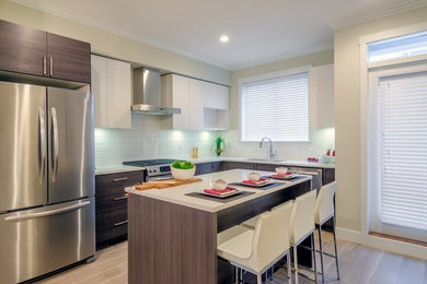 Mid-sized trendy l-shaped laminate floor eat-in kitchen photo in San Diego with a drop-in sink, flat-panel cabinets, white cabinets, quartz countertops, green backsplash, glass tile backsplash, stainless steel appliances and an island