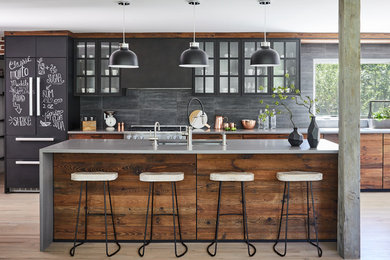Inspiration for a large industrial galley eat-in kitchen in New York with an undermount sink, flat-panel cabinets, dark wood cabinets, grey splashback, black appliances, light hardwood floors, with island, beige floor and grey benchtop.
