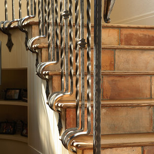 Modelo de escalera tradicional con contrahuellas de terracota, barandilla de metal y escalones de madera