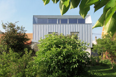 Exemple d'une façade de maison de ville métallique et grise tendance en planches et couvre-joints de taille moyenne et à deux étages et plus avec un toit à deux pans, un toit en métal et un toit gris.