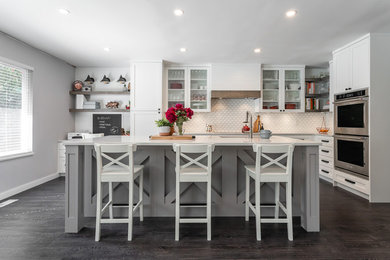 Country l-shaped dark wood floor and brown floor kitchen photo in Vancouver with white cabinets, white backsplash, stainless steel appliances, an island, white countertops and glass-front cabinets