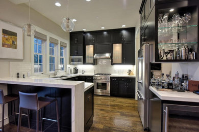 Mid-sized arts and crafts u-shaped dark wood floor and brown floor kitchen photo in San Francisco with an undermount sink, shaker cabinets, black cabinets, quartz countertops, white backsplash, subway tile backsplash, stainless steel appliances, a peninsula and white countertops