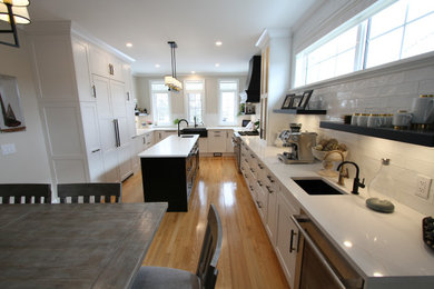 Large trendy u-shaped light wood floor and beige floor eat-in kitchen photo in Toronto with a farmhouse sink, shaker cabinets, white cabinets, quartz countertops, white backsplash, subway tile backsplash, stainless steel appliances, an island and white countertops